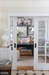 Striped walls with french doors looking into a home office with a black desk and woven rug