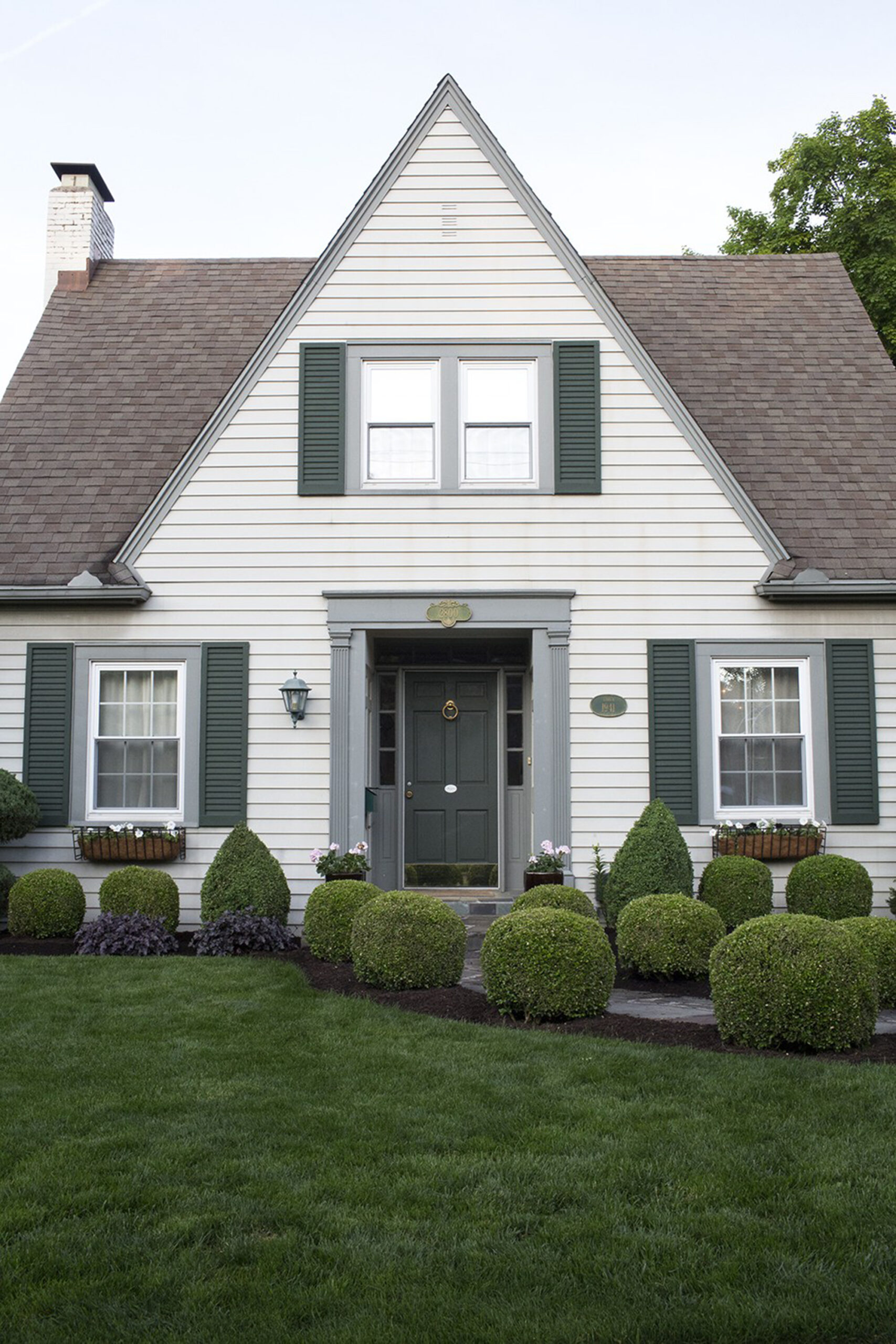 Exterior photo of a beautiful tudor house with pristine landscaping and rows of nicely manicured boxwoods lining the sidewalk.