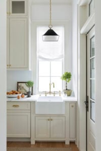 Butler's pantry with cream colored cabinetry, a black pendant, white sink, brass faucet, and hardwood floors with marble counters