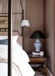 Bedside vignette with neatly hidden sconce cord, table lamp, and antique nightstand in maroon color blocked bedroom