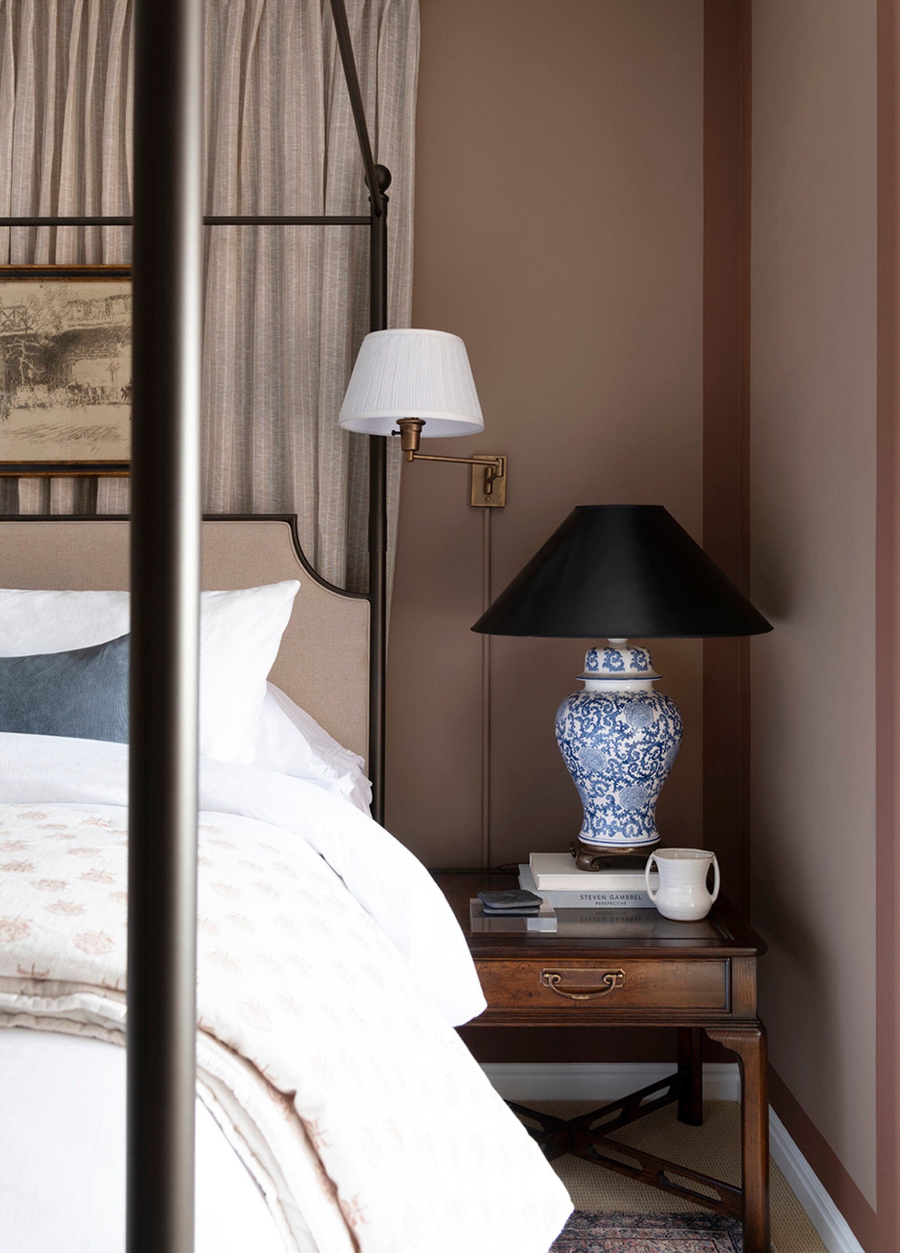 Bedside vignette with neatly hidden sconce cord, table lamp, and antique nightstand in maroon color blocked bedroom