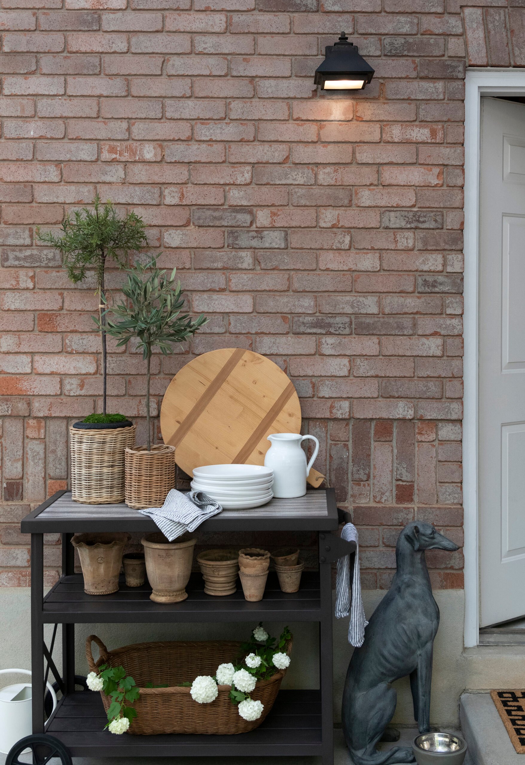 Faux topiary plants on an outdoor bar cart in front of a brick exterior
