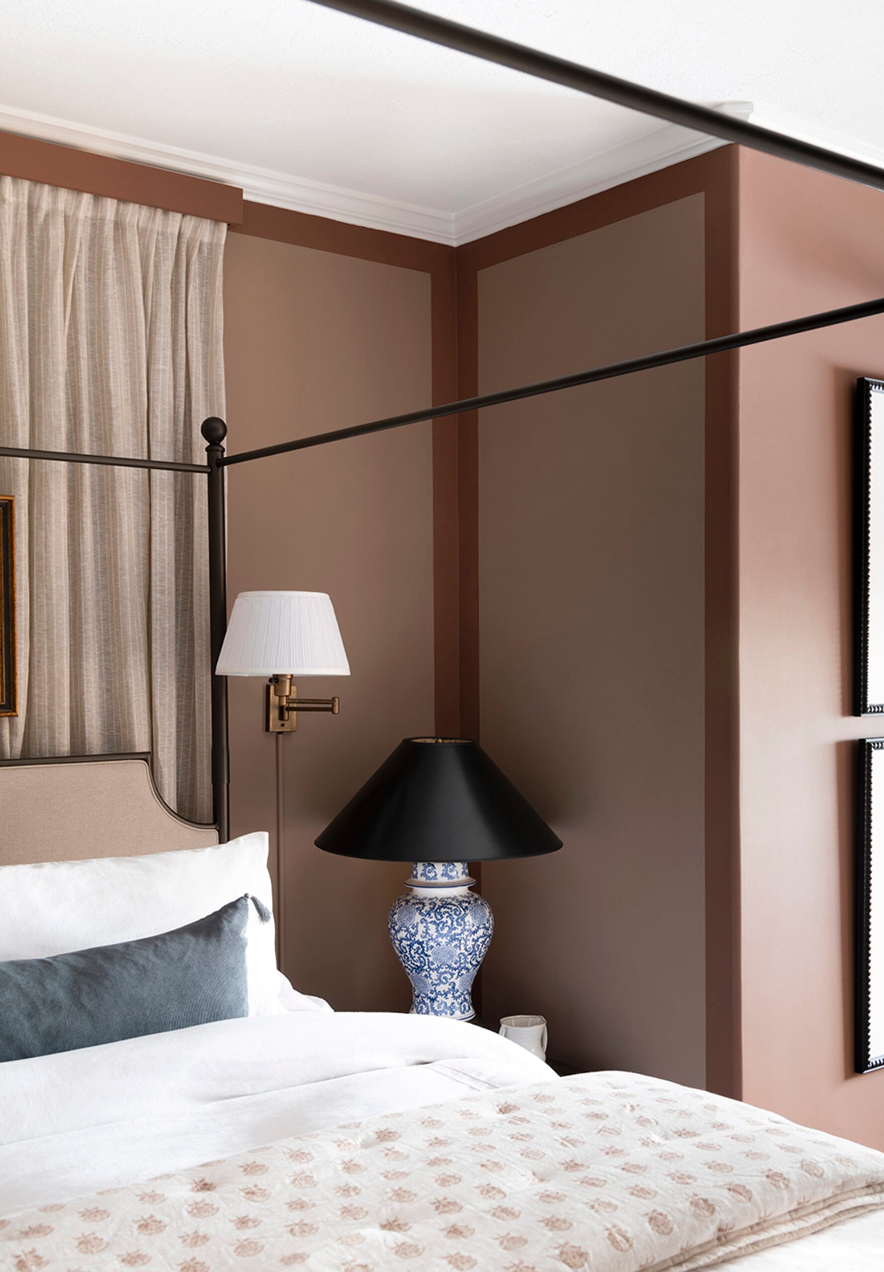 Maroon bedroom with four posted bed, blue and white table lamp, brass sconce with a hidden cord, and a block print quilt