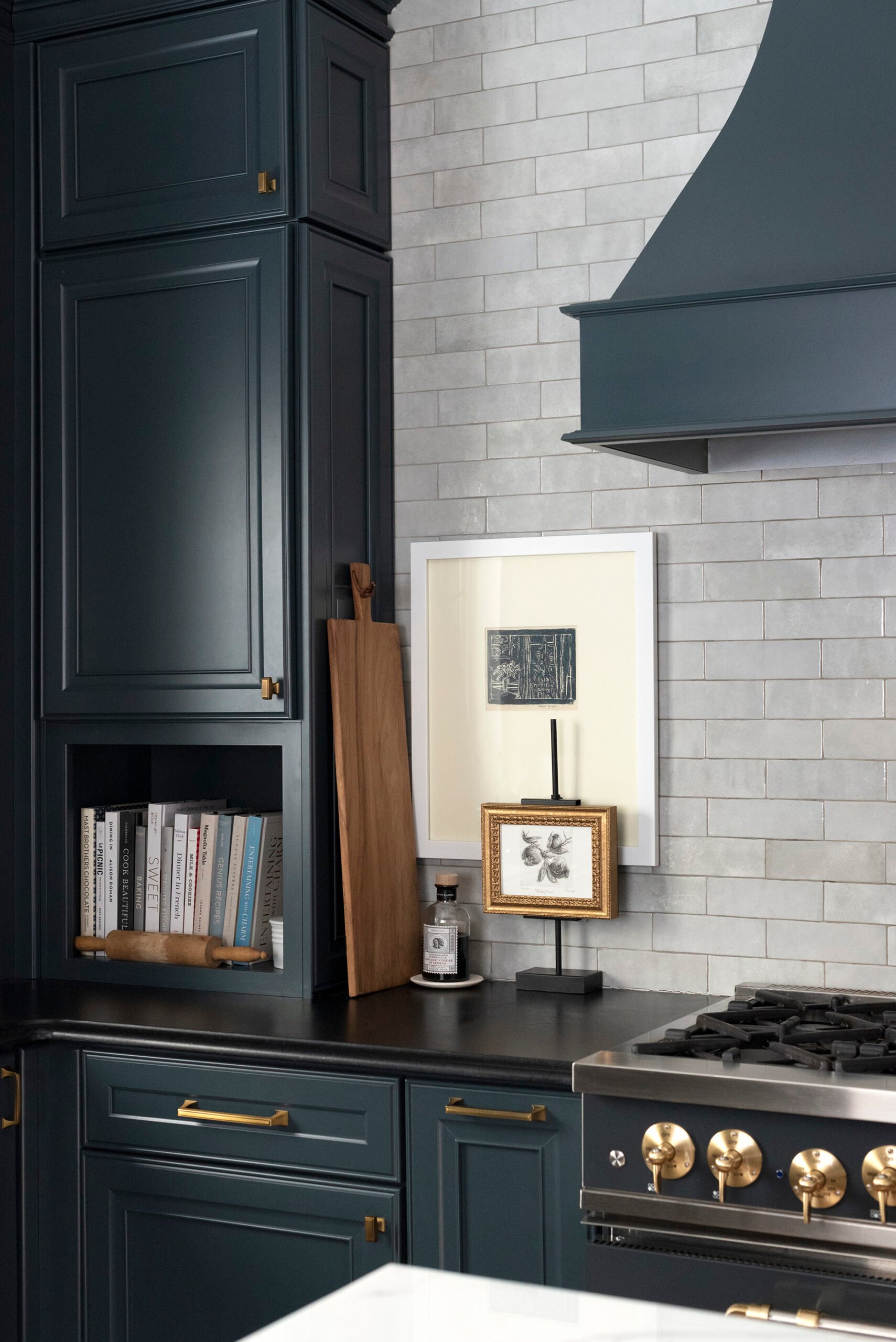 Dark navy kitchen cabinets with black soapstone countertops, artwork, cookbooks, and a french styled countertop