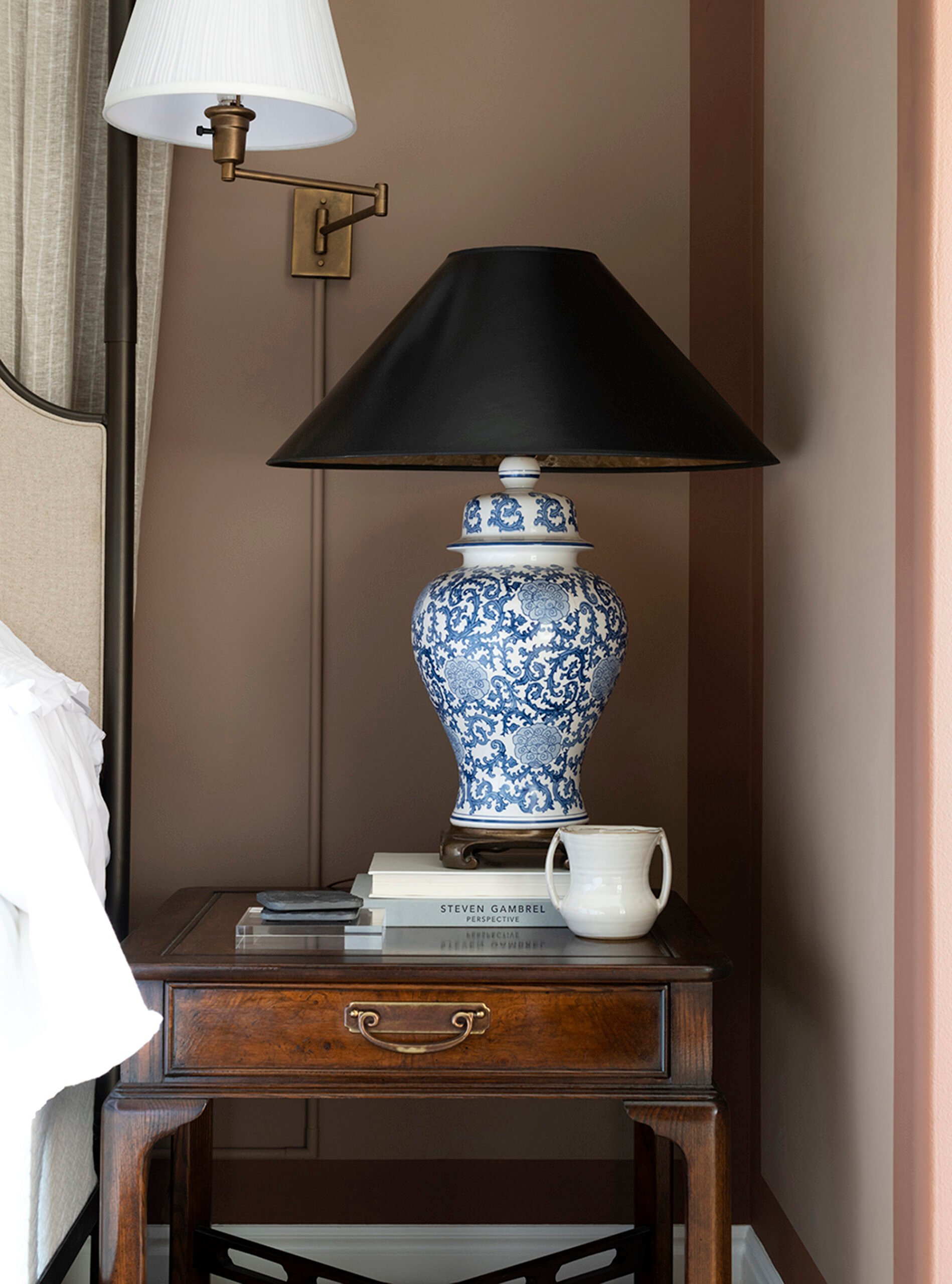 Antique nightstand, blue and white table lamp, and brass sconce with concealed cord styled a bedside