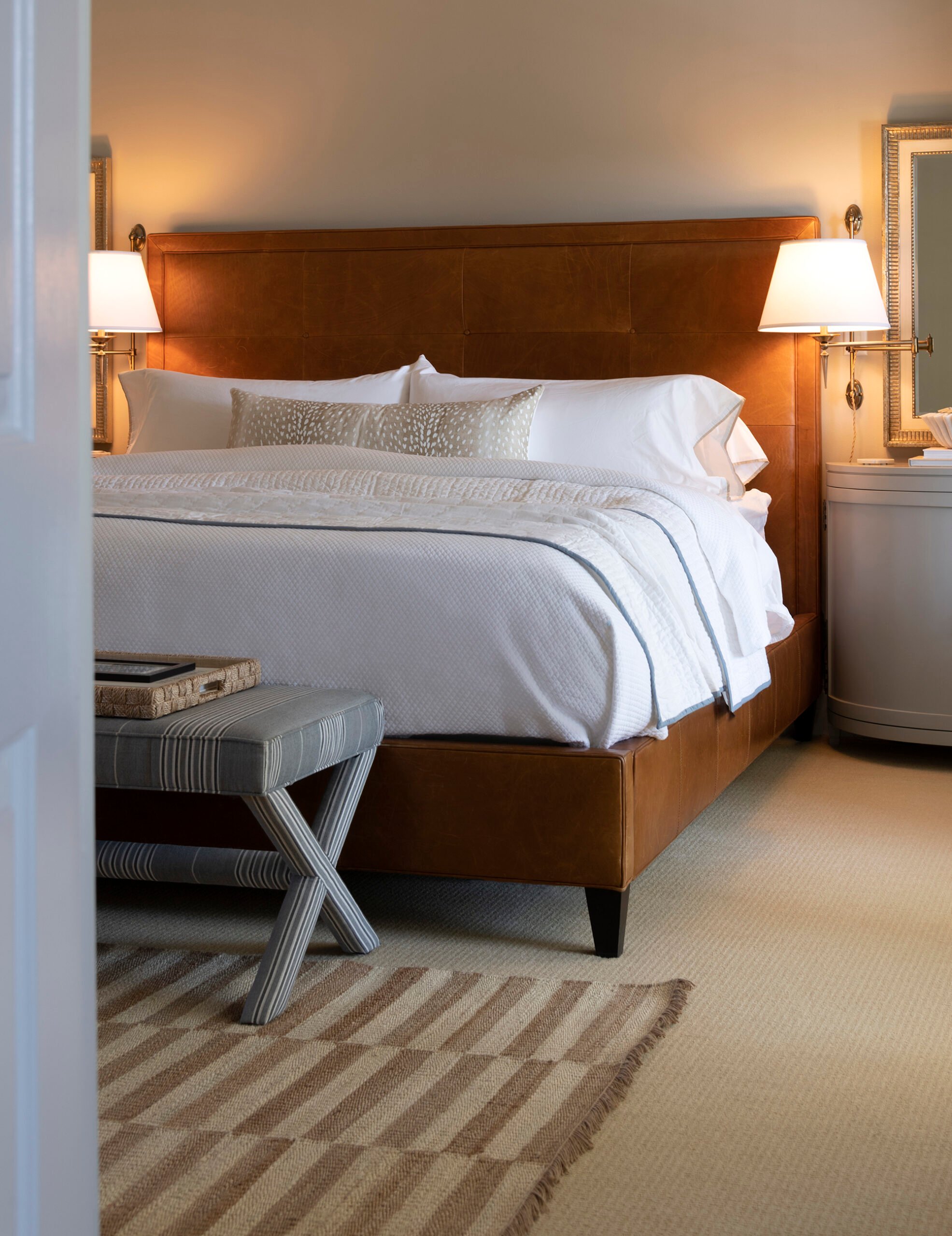Leather upholstered bed with classic white bedding and bedside sconces