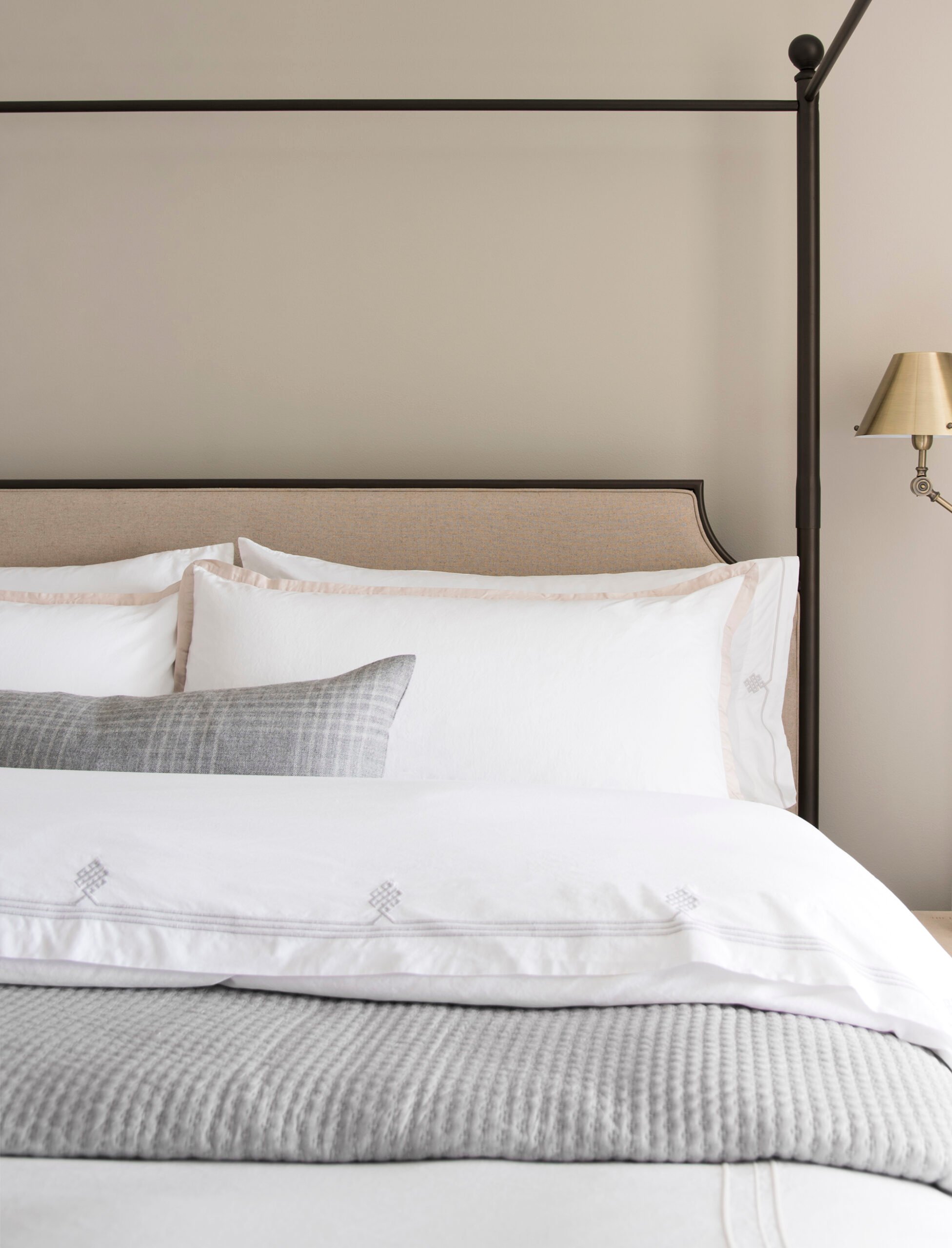 Neutral canopy bed with classic white bedding and brass bedside sconce