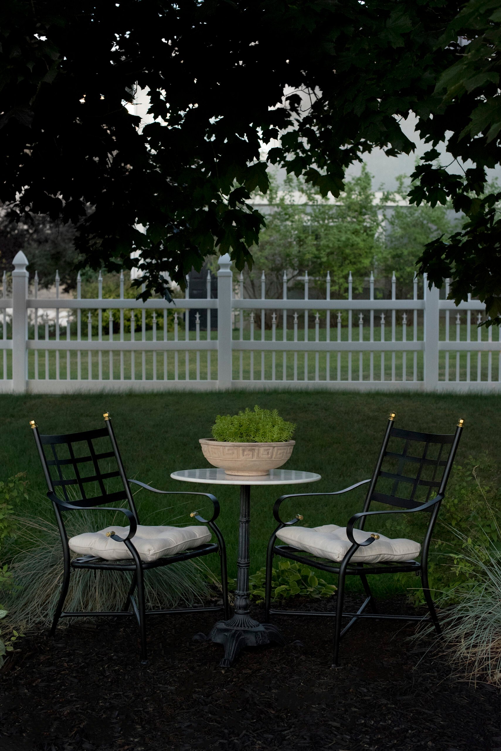 Pair of wrought iron patio chairs with gold details and french cushions under a shade tre
