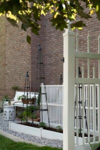 Side yard garden with marble chip gravel, a raised beds, concealed HVAC units, potted plants, and a bench