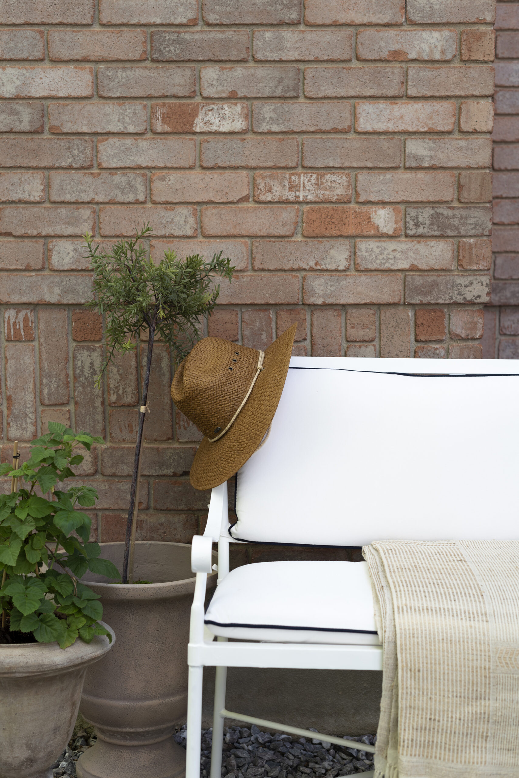Terracotta planters styled by garden bench in front of a brick wall