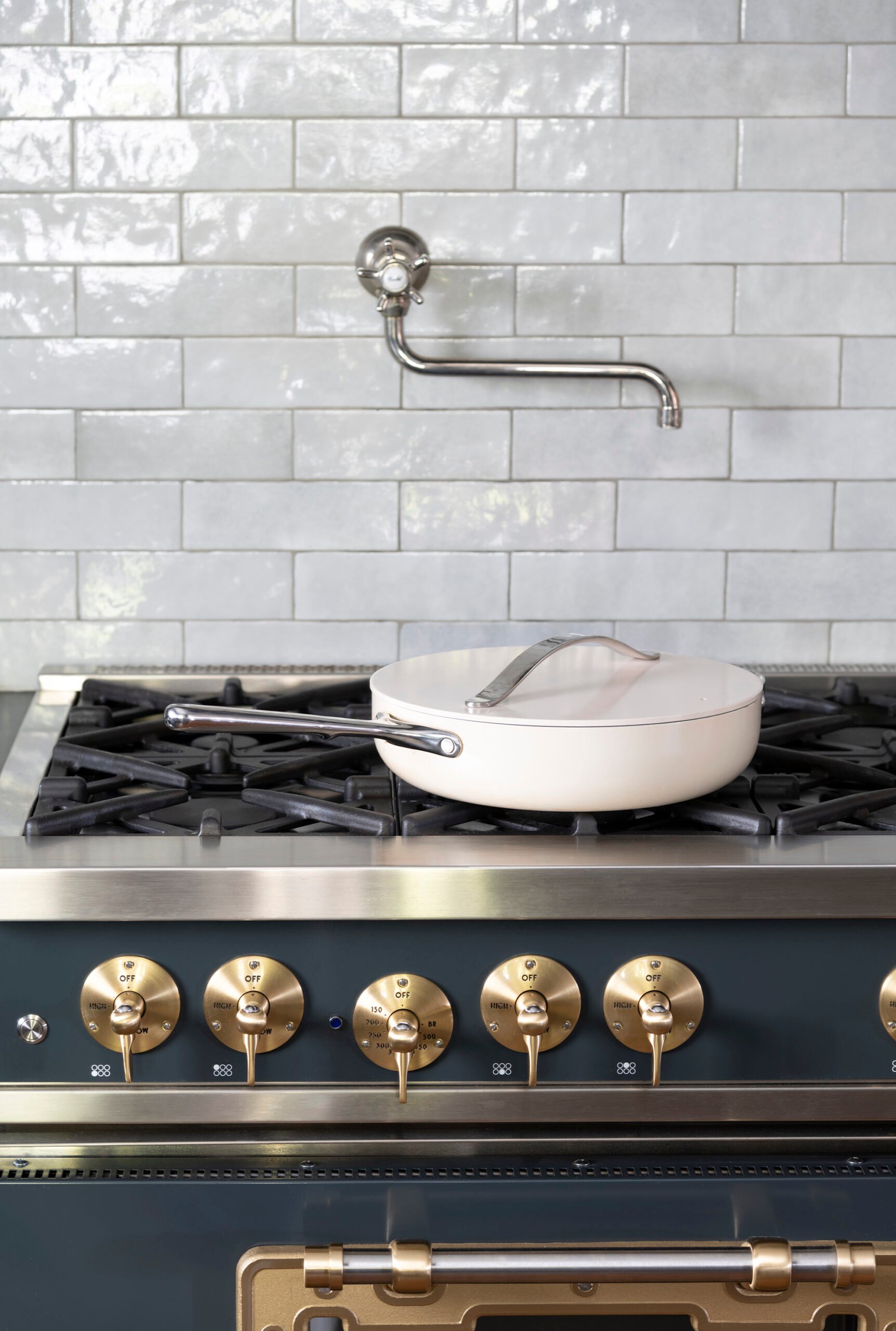 Caraway frying pan on gas range with brass knobs and gray backsplash tile