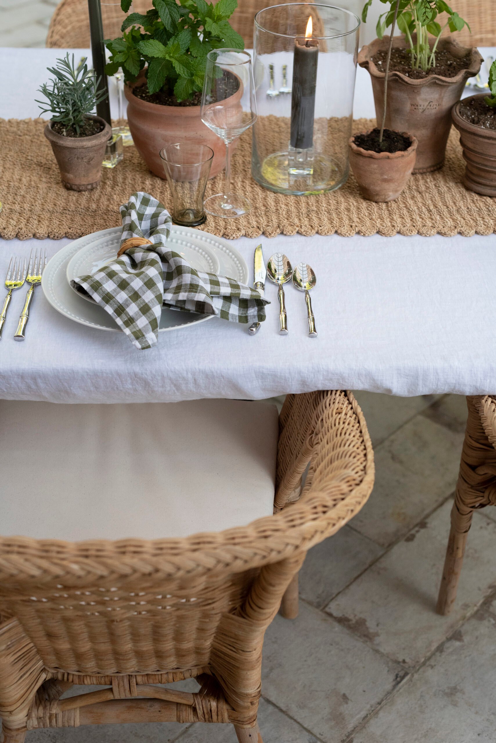 Using terracotta planters as a tablescape centerpiece with a woven table runner and white linen tablecloth