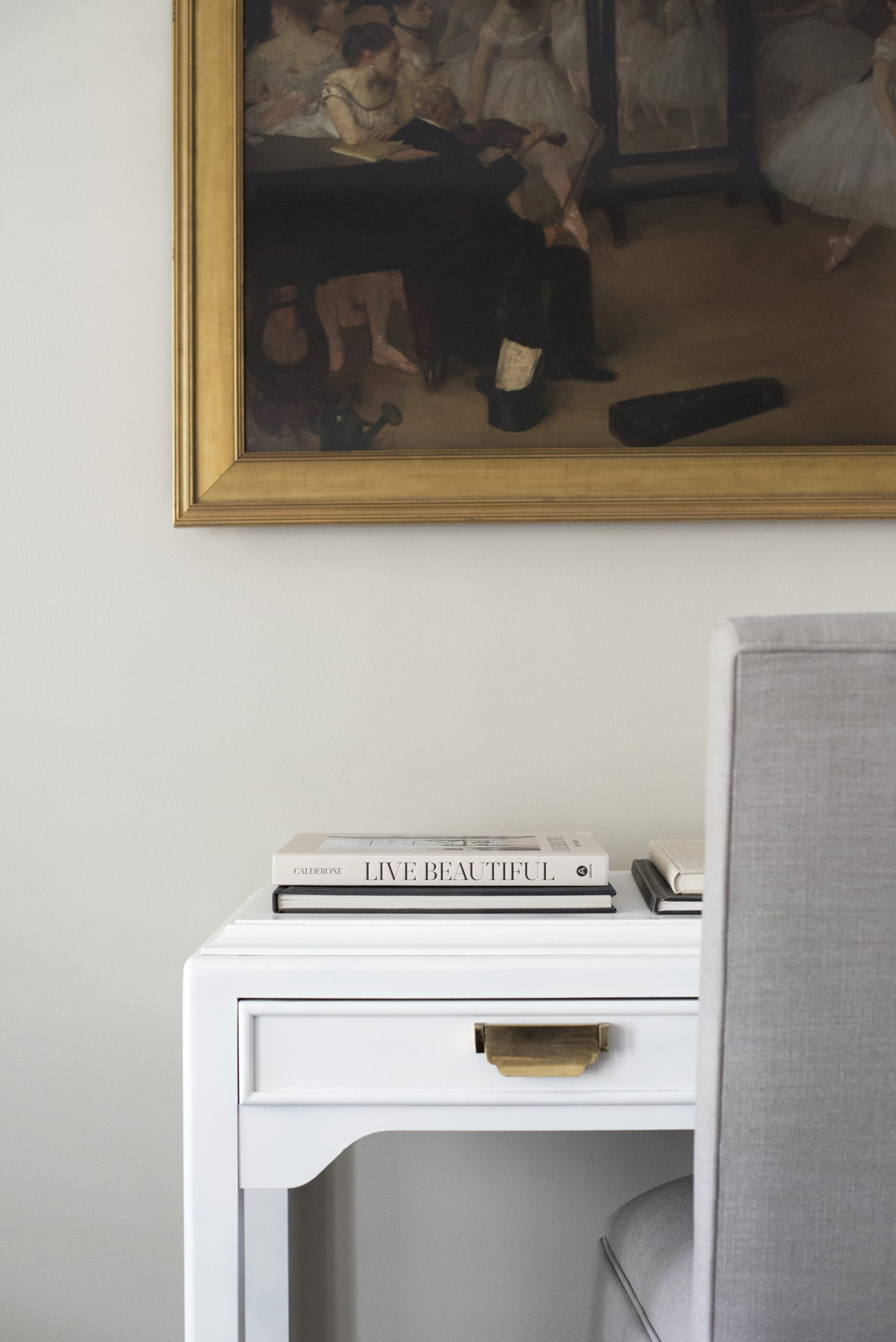 White enamel desk with brass hardware under large framed art