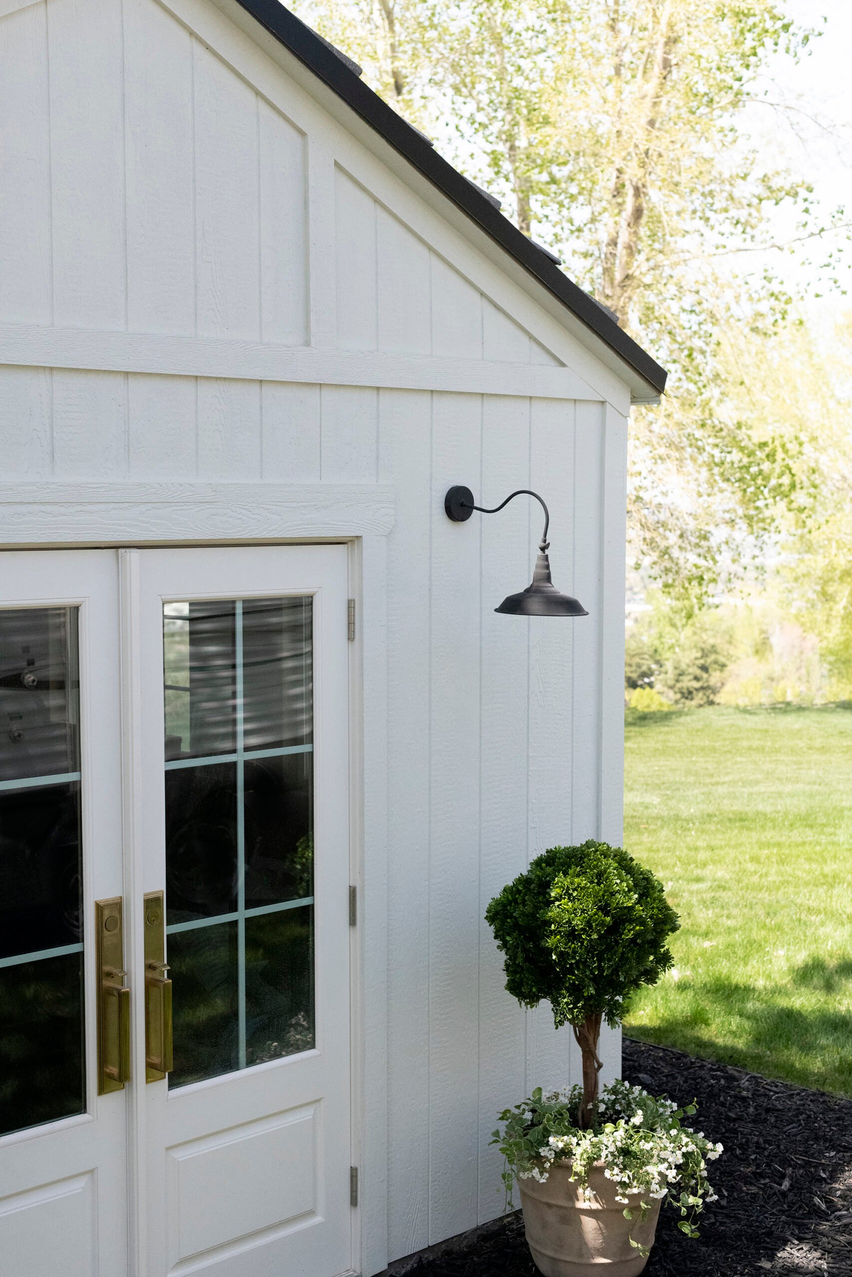White storage shed with faux boxwood topiary in terracotta planter and brass door hardware