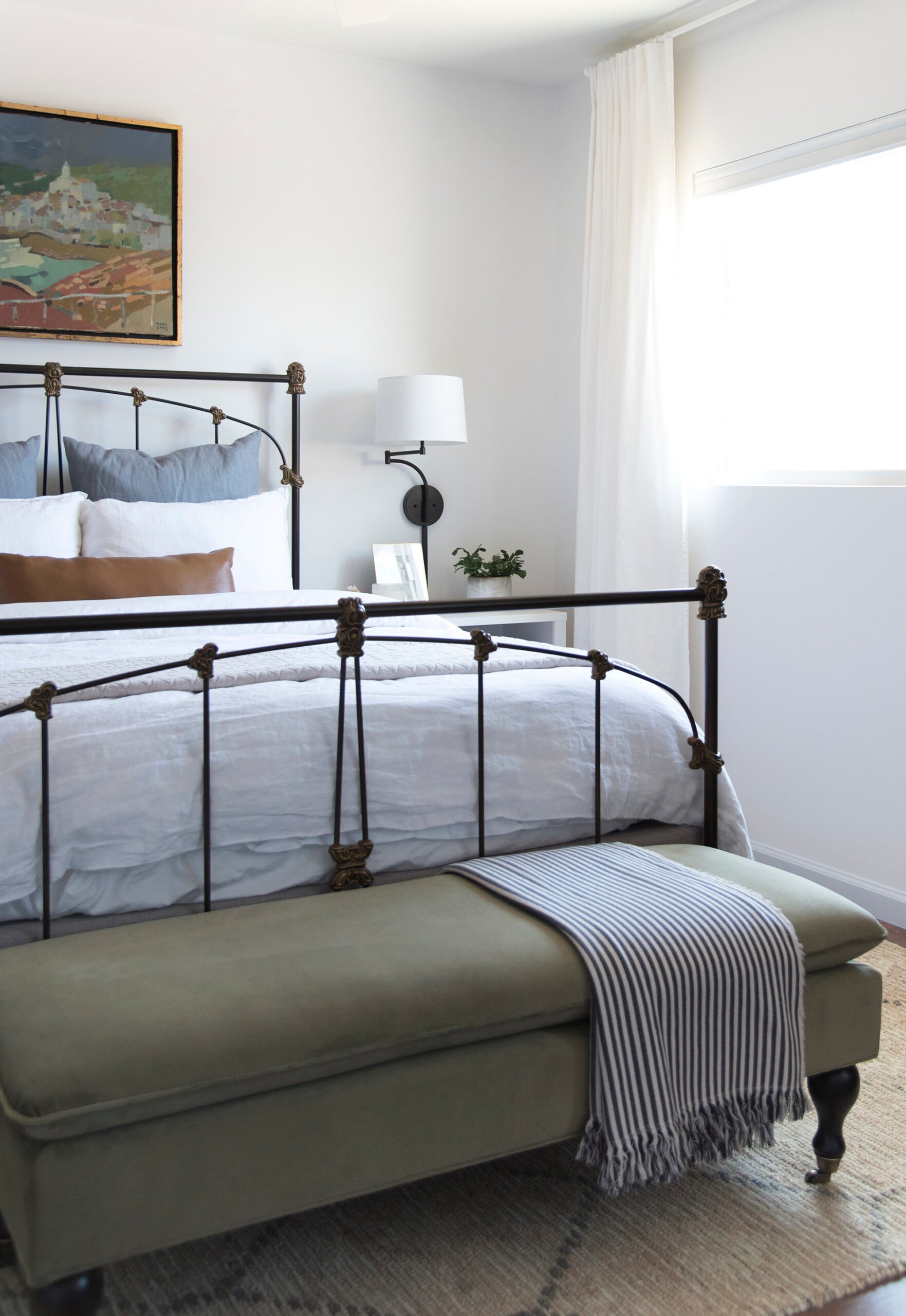 Wrought iron bed frame with green bench and woven rug